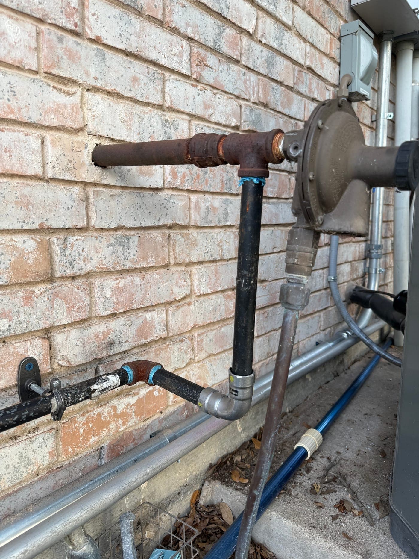 A gas line and sediment trap run along a brick wall to a home standby generator, strapped and supported to code.